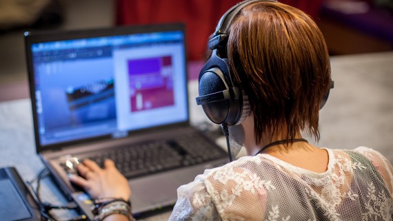 Een meisje met koptelefoon zit achter een laptop