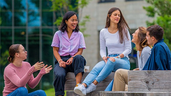 Vijf studenten zitten op houten blokken op de BUas campus