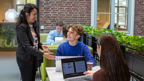 Een docent staat bij twee studenten met laptops aan een tafel