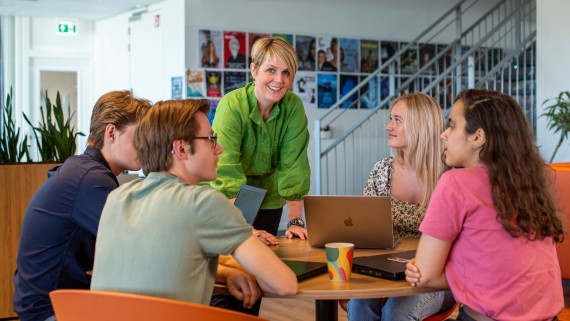 Een docent staat bij een tafel met vier studenten