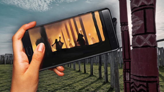 Hand met een telefoon met daarop een monument van palen