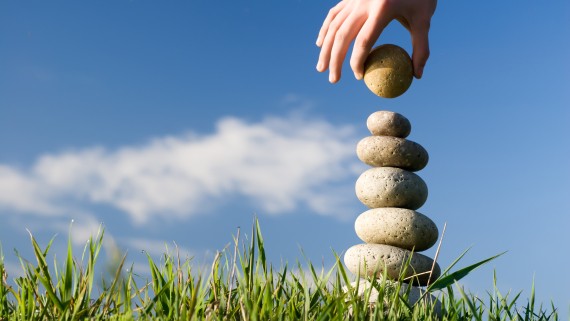 Een hand bouwt een toren van stenen in het gras
