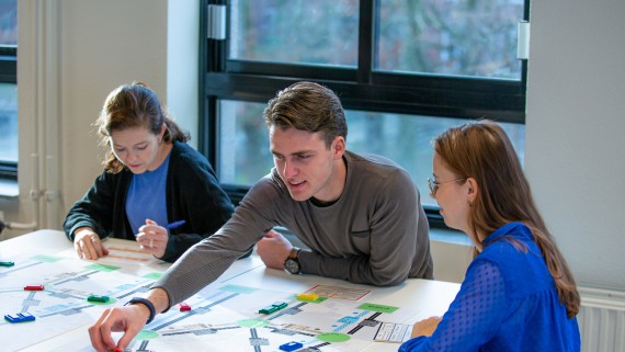 Drie studenten logistiek werken aan een tafel met kaarten