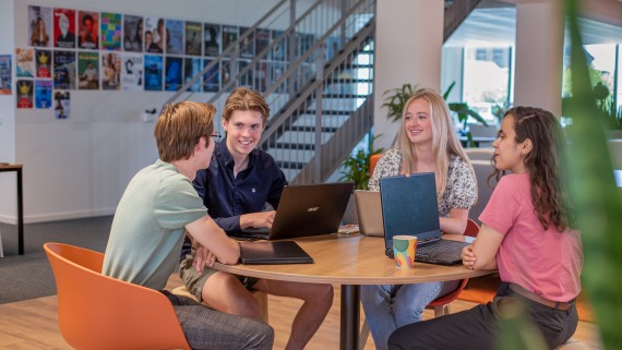 Vier studenten werken samen op laptops aan een tafel