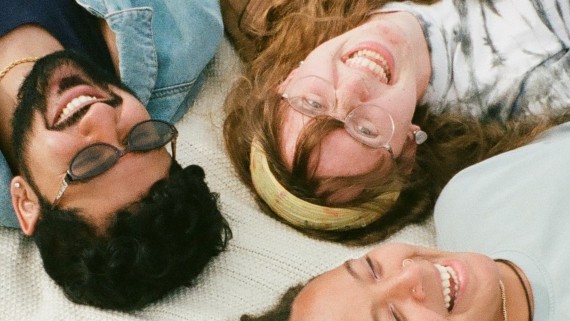 Drie studenten liggen op een kleed in het gras