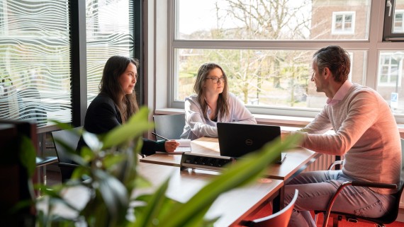 Een docent zit aan tafel met twee studenten