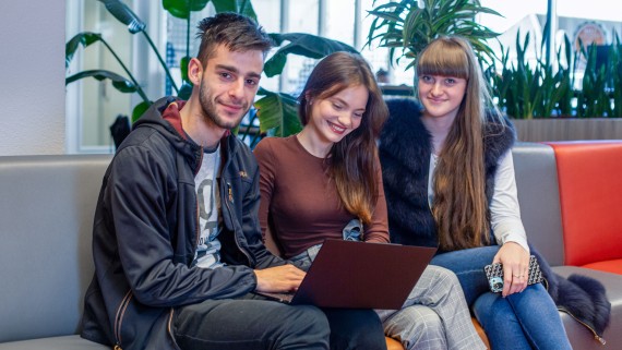 Drie studenten zitten met een laptop op een bank