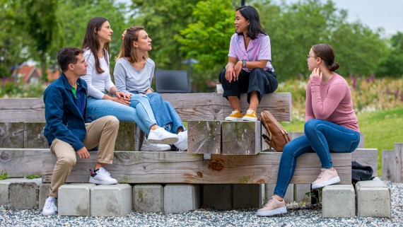 Vijf studenten zitten op een bank op de BUas campus