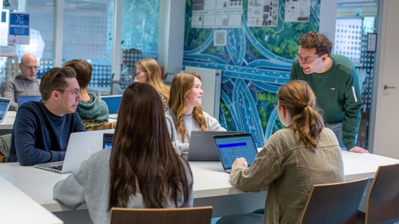 Een docent staat bij studenten aan een tafel 