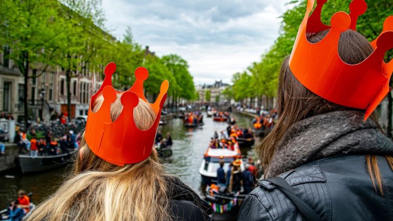 Twee meisjes met een oranje kroon kijken naar varende boten