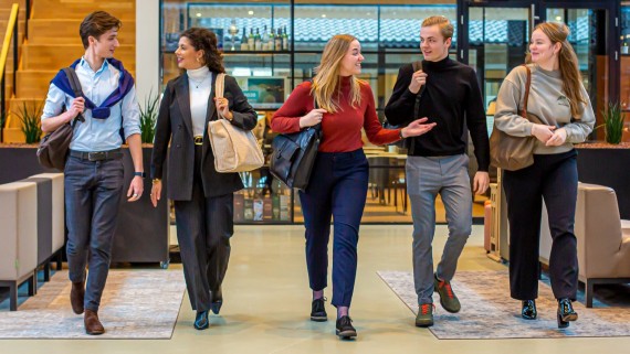 Vijf studenten lopen met hun tassen door de school