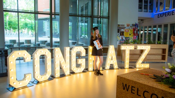 Een afgestudeerde student poseert voor de letters 'Congratz'