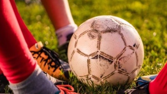 Vier voeten met voetbalschoenen staan naast een voetbal