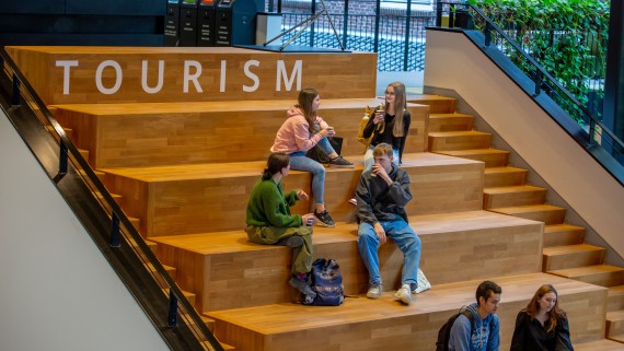 Studenten zitten te kletsen op een trap binnen het buas gebouw