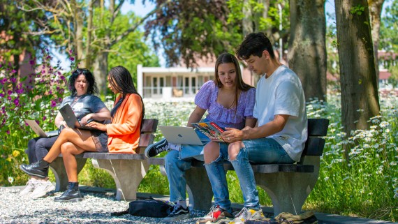 Vier studenten zitten op een bankje buiten op de BUas campus