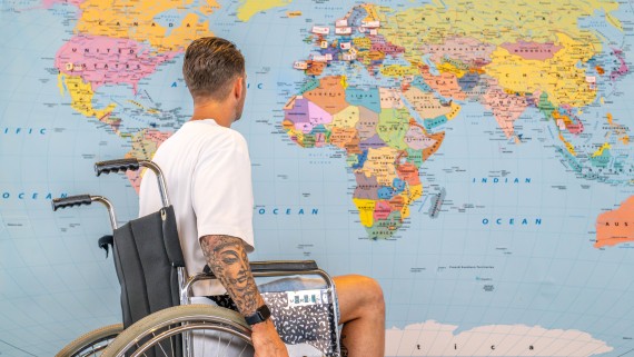 Man in rolstoel voor een grote wereldkaart