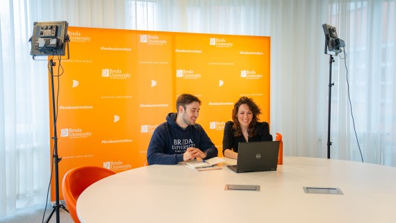 two people with laptop in front of orange screen