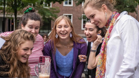 five students laughing while looking at video on their phone