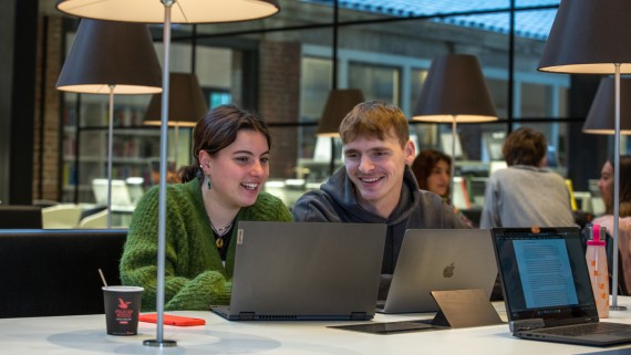 Twee studenten lachen samen achter een laptop