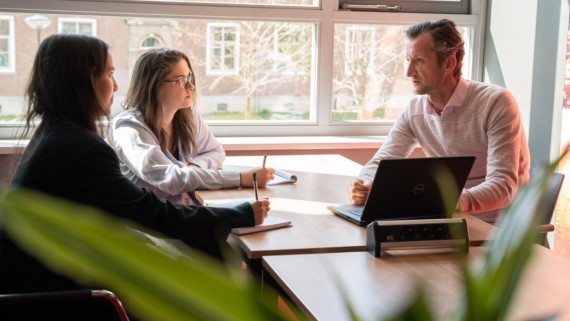 Twee studenten praten met een docent over hun werk