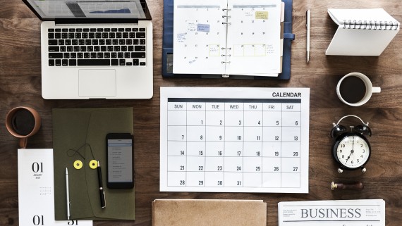 Een tafel met kantoorspullen, een kalender, krant en klok