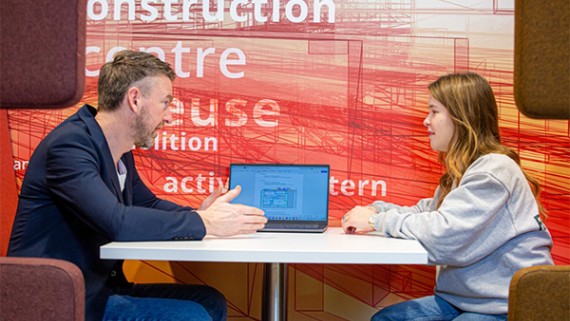 Een docent zit aan een tafel met een student 