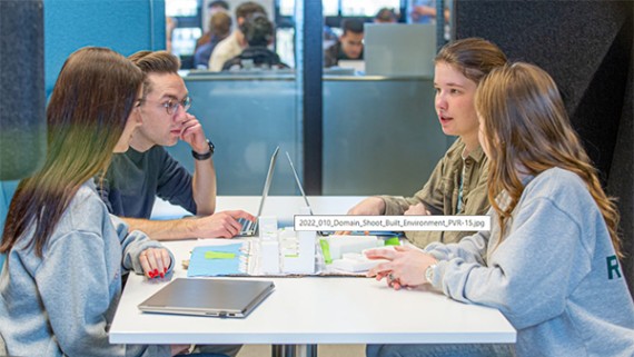 Vier studenten aan een tafel werken samen aan een project 