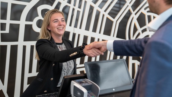 Een vrouw achter een balie geeft een man een hand