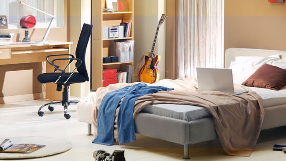 Een rommelige slaapkamer met een bed, bureau en stoel