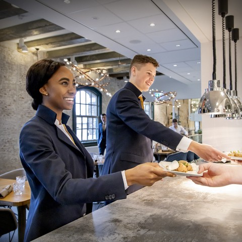 Twee horeca studenten geven een bord aan iemand anders
