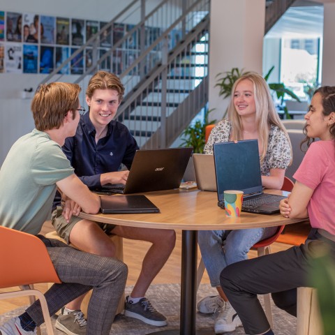 Vier studenten werken samen op laptops aan een tafel