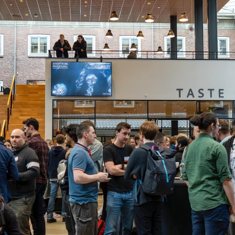 Een grote groep mensen praat aan statafels 