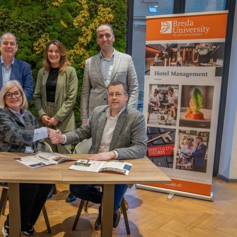 Twee mensen schudden de hand en drie staan erachter