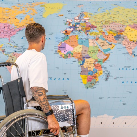 Man in rolstoel voor een grote wereldkaart