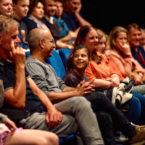 Een publiek zit op stoelen in een zaal