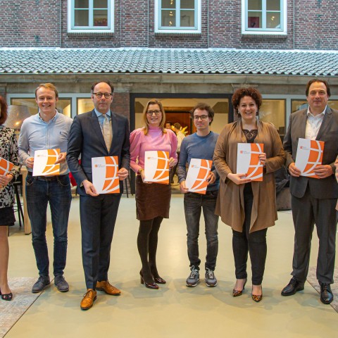 Groepsfoto van acht mensen met een document in hun handen