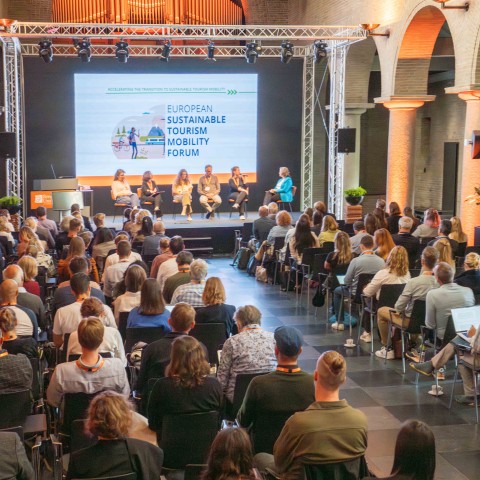Een zaal vol deelnemers luistert naar sprekers op het podium