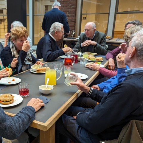 Ouderen lunchen samen aan grote tafels