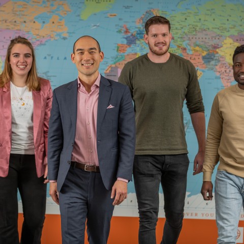 Groepsfoto van vier studenten voor een wereldkaart