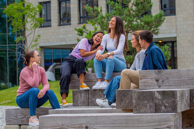 Vijf studenten zitten op houten blokken op de BUas campus
