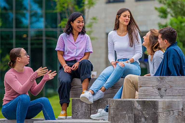 Vijf studenten zitten op houten blokken op de BUas campus