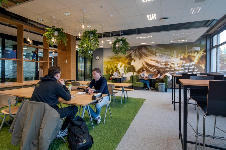 Studenten met laptops werken samen aan tafels 