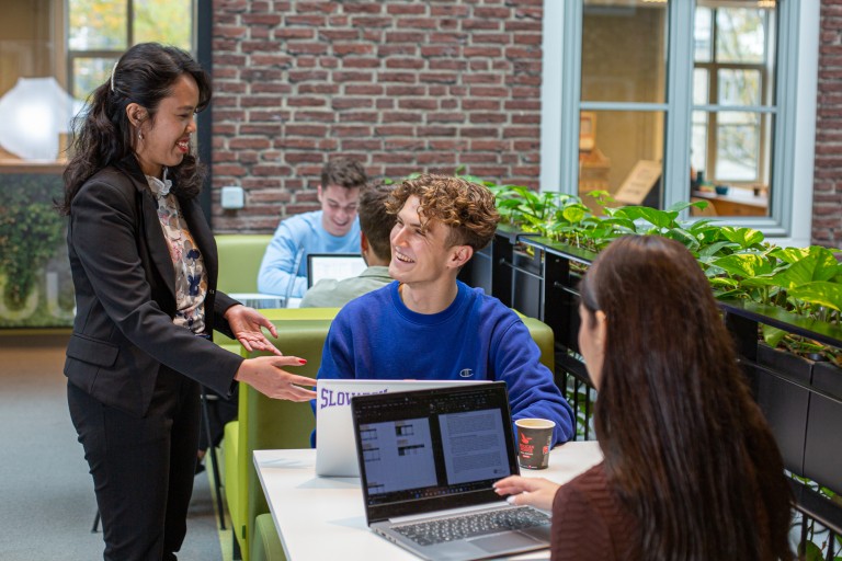 Een docent staat bij twee studenten met laptops aan een tafel
