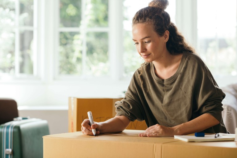 Een vrouw schrijft iets op een ingepakte verhuisdoos