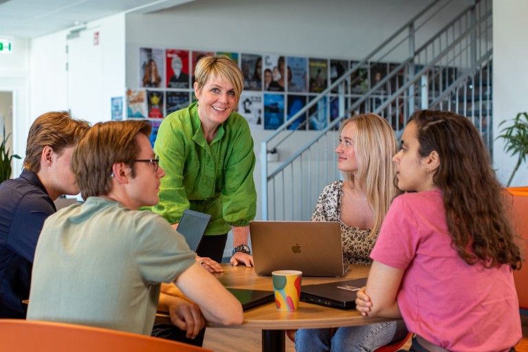 Een docent staat bij een tafel met vier studenten
