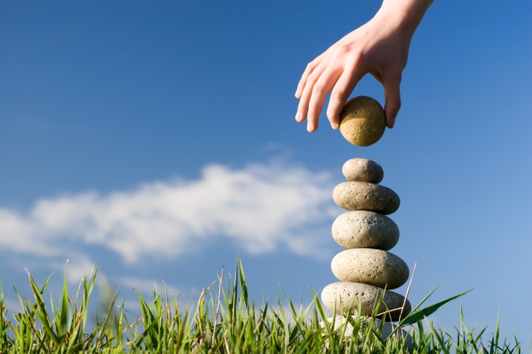 Een hand bouwt een toren van stenen in het gras