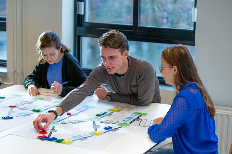 Drie studenten logistiek werken aan een tafel met kaarten