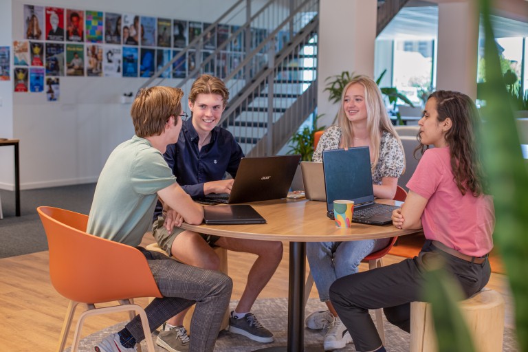 Vier studenten werken samen op laptops aan een tafel
