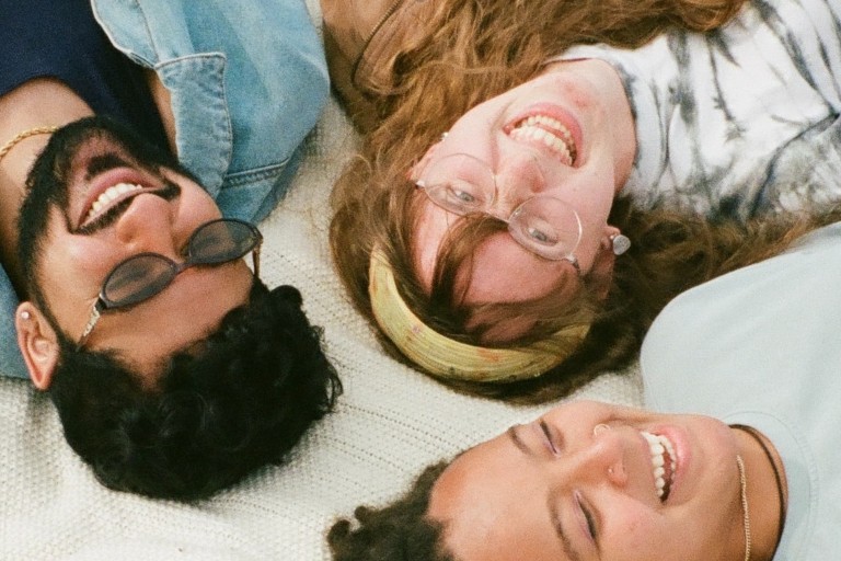 Drie studenten liggen op een kleed in het gras