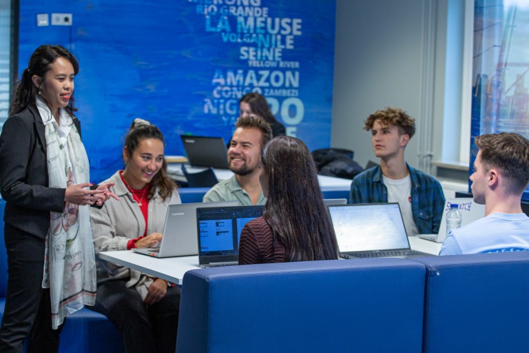 Een docent legt iets uit aan vijf studenten aan een tafel